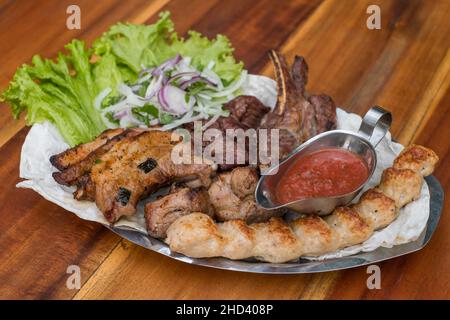 Assorted delicious grilled meat with lettuce and onion. Mixed grilled bbq meat with tomato sauce.Lamb, chicken. Top view, close up with copy space. Stock Photo