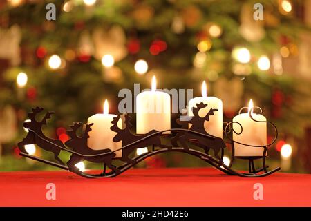 Table Decoration with Four Advent Candles on Reindeer Candle Holder in Front of Christmas Tree Lights Stock Photo
