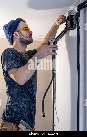 An electrician is mounting electric sockets on the white wall indoors. Stock Photo