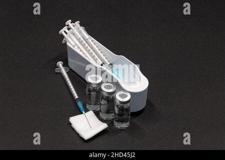 Medical Equipment that includes Syringes with Hypodermic Needles with Safety Caps and vials Containing a clear Liquid. Stock Photo