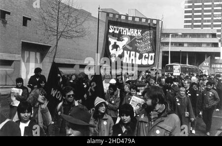 A 1984 demonstration march by members of the Southwark branch of the British trade union, NALGO (National and Local Government Officers' Association) protesting against the planned abolition of the GLC (Greater London Council). The photograph depicts the marchers passing by the National Theatre, Upper Ground, Southwark, London. The protestors are carrying the Southwark Branch NALGO banner, placards with the slogans, “Hands off Local Govt”, “Hands off The GLC” and also copies of the feminist newspaper ‘Outwrite’ bearing the headline, “Miners Wives – Media Lies”. Stock Photo