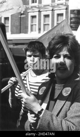 Two female protestors attending a demonstration organised by the Southwark branch of the British trade union, NALGO (National and Local Government Officers' Association) and Southwark Trades Council, protesting against the dismissal of a worker from Southwark London Borough Council. Mid 1980s. The photograph depicts the protestors holding placards, marching along Walworth Road, Southwark, passing The Rock pub. The woman in foreground is wearing sticker badges on her coat lapels, bearing the slogan, “Friday 13th Unlucky for Southwark? Rally – 12 Noon”. Stock Photo