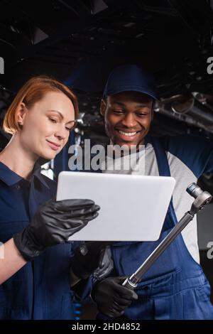 Multiethnic mechanics with digital tablet and wrench standing near car in garage Stock Photo