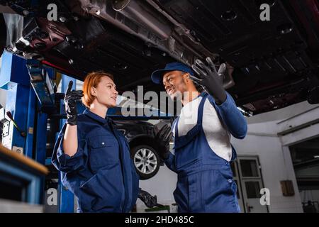 Positive interracial mechanics in gloves and uniform standing under car in service Stock Photo
