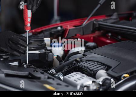 cropped view of mechanic in work gloves inspecting car engine compartment with screwdriver Stock Photo