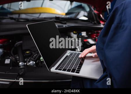 partial view of forewoman with laptop making diagnostics of blurred car in service Stock Photo