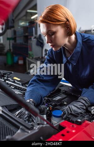 forewoman in uniform fixing motor of car in workshop Stock Photo