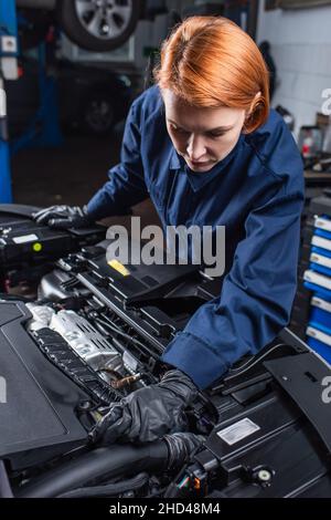 mechanic in uniform and work gloves inspecting motor of car in service station Stock Photo