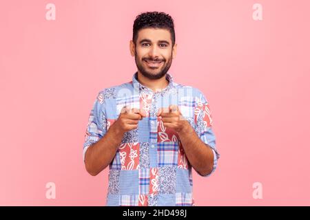 Hey you. Portrait of cheerful bearded man in blue casual style shirt pointing to camera, smiling, making happy choice, we need you concept Indoor studio shot isolated on pink background. Stock Photo