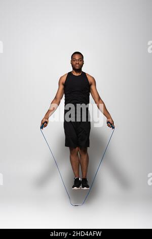 full length of african american sportsman jumping with skipping rope on grey Stock Photo