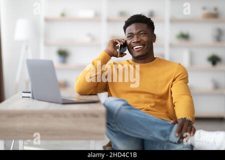 Cheerful man sitting at table with laptop, talking on phone Stock Photo