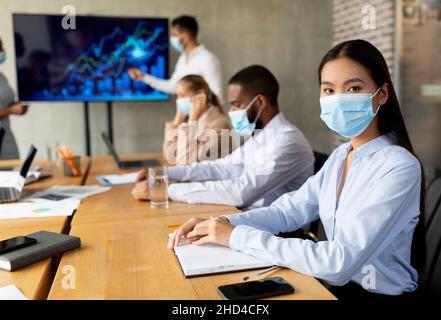 COVID-19 Office Safety. Diverse Business People In Medical Masks Attending Corporate Meeting Stock Photo