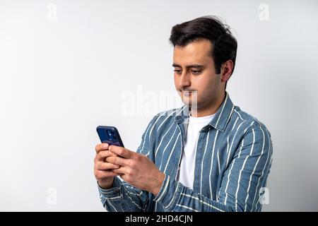 Close up photo of a brown skinned young adult model, texting with friends on social media with smartphone on isolated white background. Stock Photo