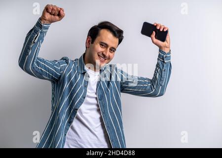 Close up photo of a brown skinned young adult model, making instant happy expression while holding smartphone on isolated white background. Stock Photo