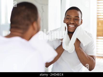 Male Beauty Care. Smiling African American Man Wiping Face With Towel In Bathroom Stock Photo