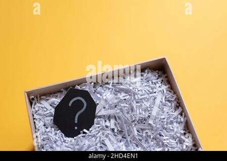 Question mark and shredded paper in abox against yellow background. Concept of Questions, recycle and secret Stock Photo