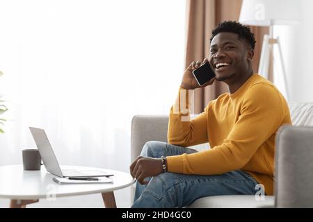Positive black guy working from home, having phone conversation Stock Photo