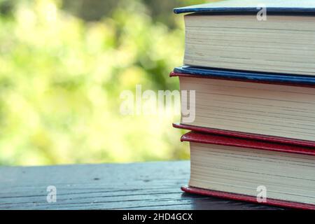 Three old books close up on a wooden garden table outdoors, green background, copy space Stock Photo