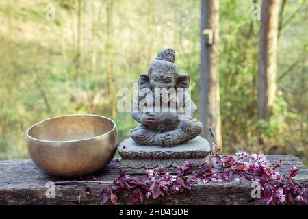 Singing bowl made of seven metals and Ganesh deyty decorative stone statue in the garden. Stock Photo