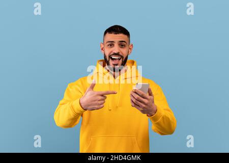 Mobile offer. Excited arab man pointing at smartphone in his hands, emotionally reacting to cool app or website Stock Photo