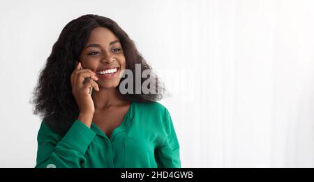 Cheerful african american woman standing by window, talking on phone Stock Photo