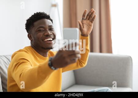 Cheery black man having online party with friends, using smartphone Stock Photo