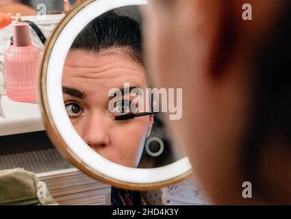 Portrait of young woman doing her make-up in front of circular led illuminated mirror Stock Photo