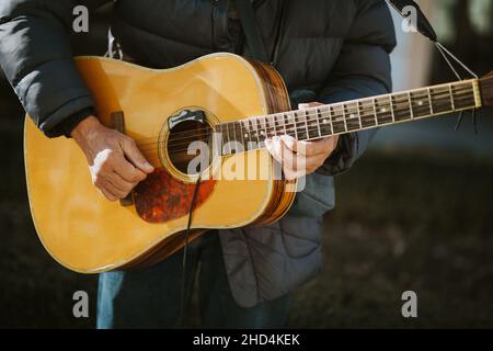 Closeup shot of a man with jacket holding guitar and playing music Stock Photo