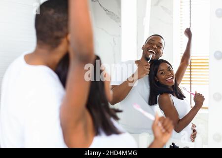 Joyful Black Couple Singing And Dancing While Brushing Teeth In Bathroom Stock Photo
