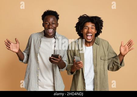 Mobile Offer. Portrait Of Two Excited Black Friends With Smartphones In Hands Stock Photo