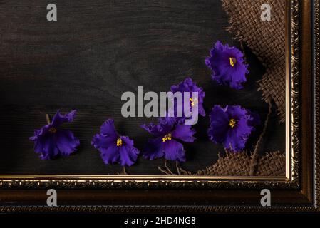 Part of a beautiful frame contains rough weave fabric on a wooden background and violet flowers. Background for the inscription. Stock Photo