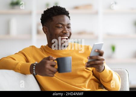 Happy african american guy reclining on couch, using smartphone Stock Photo