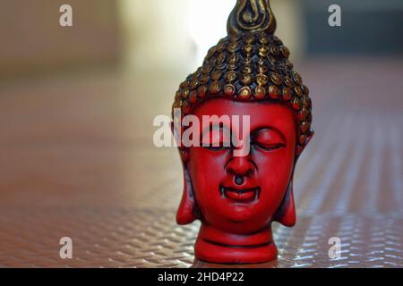 Stock photo of beautiful red color face sculpture or statue of lord buddha, head of statue painted with black and golden color on brown color backgrou Stock Photo