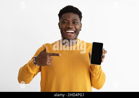 Laughing african american guy in casual pointing at smartphone, mockup Stock Photo