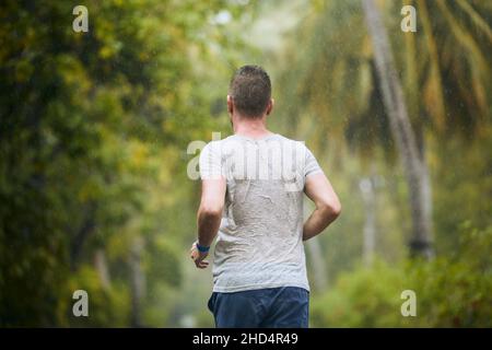 Rear view of runner in heavy rain. Drenched young man runing in nature. Stock Photo