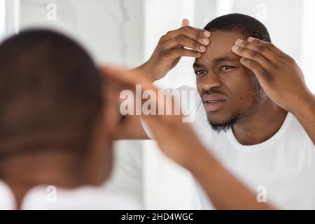 Problem Skin. Concerned Black Guy Inspecting Face, Noticed Pimple On Forehead Stock Photo