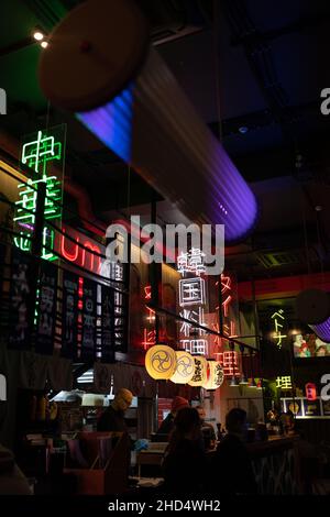 People eating in trendy modern chinese restaurant decorated with paper lanterns and neon hieroglyphs Stock Photo