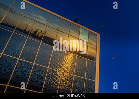 Modern glass building with reflected evening city and sunset sky in it. Sunset through window panels Stock Photo