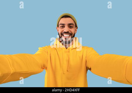 Happy middle eastern bearded man taking selfie, having fun, looking and smiling at camera, blue background Stock Photo