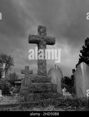 A rough stone cross headstone stands proudly against a stormy sky - Spital Cemetery, Chesterfield, North East Derbyshire Stock Photo