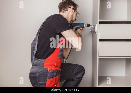 Furniture assembler drilling holes to fix sliding pants hanger in wardrobe Stock Photo