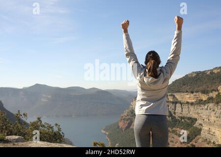 Back view portrait of a happy trekker raising arms in nature celebrating success Stock Photo