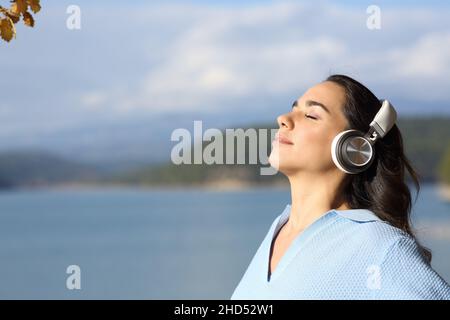 Side view portrait of a relaxed woman wearing headphones meditating in a lake