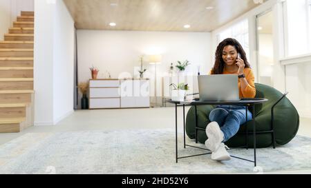 Smiling black woman working and talking on phone at home Stock Photo