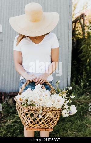 woman in large hat holds basket of freshly cut flowers Stock Photo