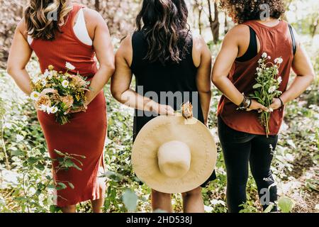 Group of women stand in forest holding flowers behind backs Stock Photo