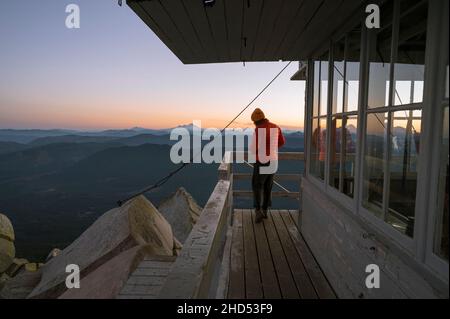 Girl standing on the deck of a fire lookout at sunset Stock Photo