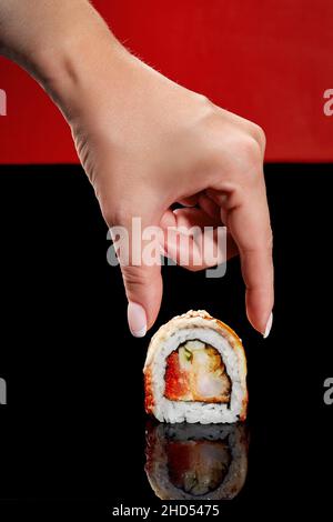 Female hand reaching out to roll with shrimp, tobiko, cucumber Stock Photo