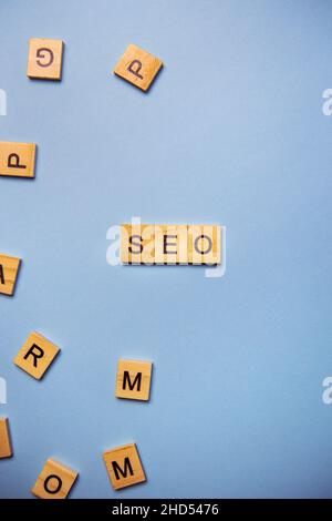 Wooden letters SEO are printed on a light blue background with many different wooden letters in the background Stock Photo
