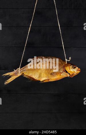 One golden smoked bream hanging on rope on black wooden Stock Photo